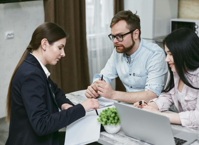 woman in a suit at a desk with papers and a laptop helping a man and a woman secure a business loan for their business