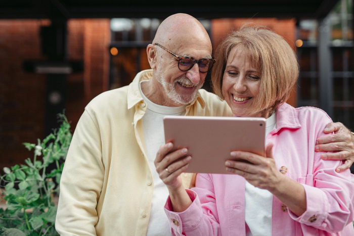 a senior couple are holding each other and smiling at a tablet