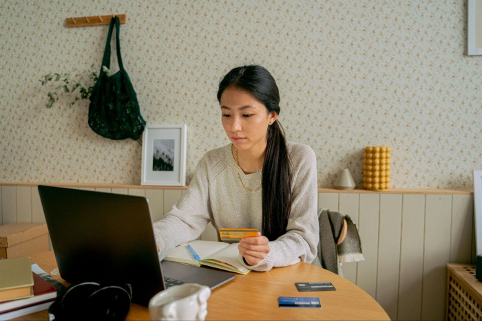 a woman looking at her debit card while on her laptop