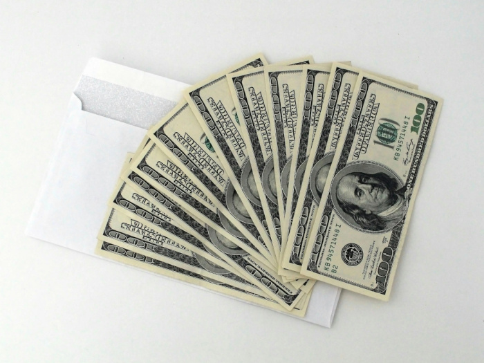 twelve 100 dollar bills laid on top of a white envelope