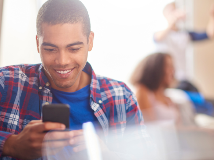 a man in a plaid shirt checking his phone excitedly to look at his essential credit union checking account