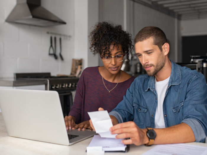 A woman and a man looking at a piece of paper and a laptop discussing their checking account in gonzales with essential credit union