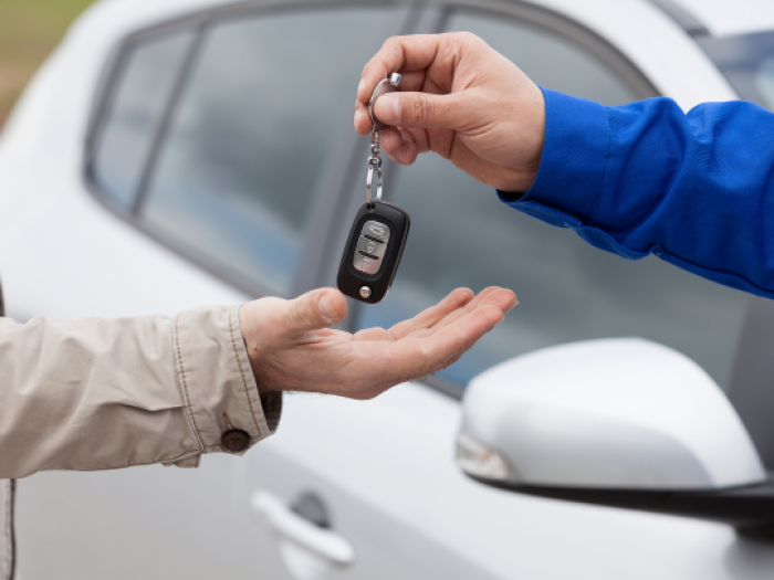 a hand in a blue sleeves hands over a car key fob to mans hand in a tan shirt after he secured his auto loan with essential credit union in walker
