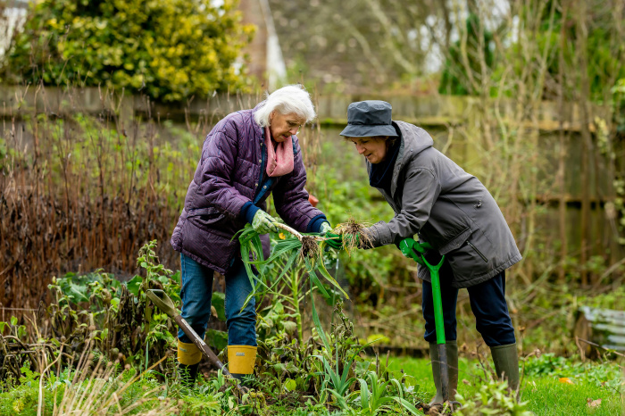 2 women with shovels planting a garden outside