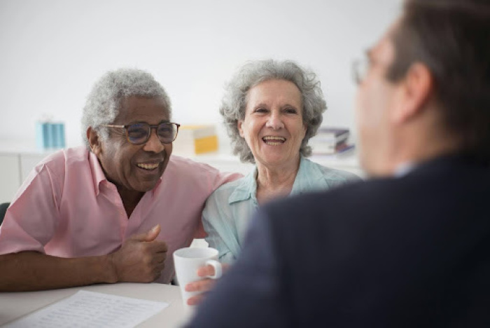 Elderly man and woman sitting next to each other laughing with banker man